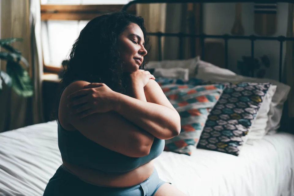 Woman hugging herself in underwear sitting on bed